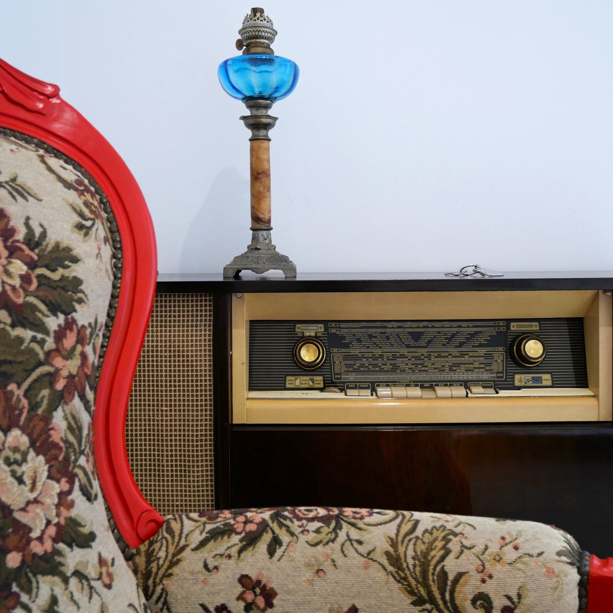 Chambre Elba : fauteuil rouge tapissé de fleurs, lampe à pétrole bleue et ancienne radio