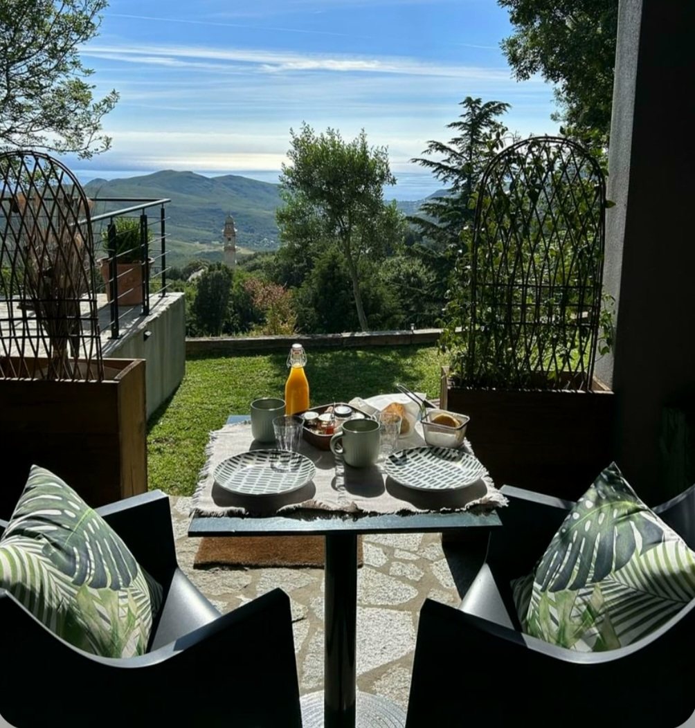 Terrasse couverte de la chambre Pianosa : table dressée pour le petit déjeuner, pelouse et vue sur la vallée